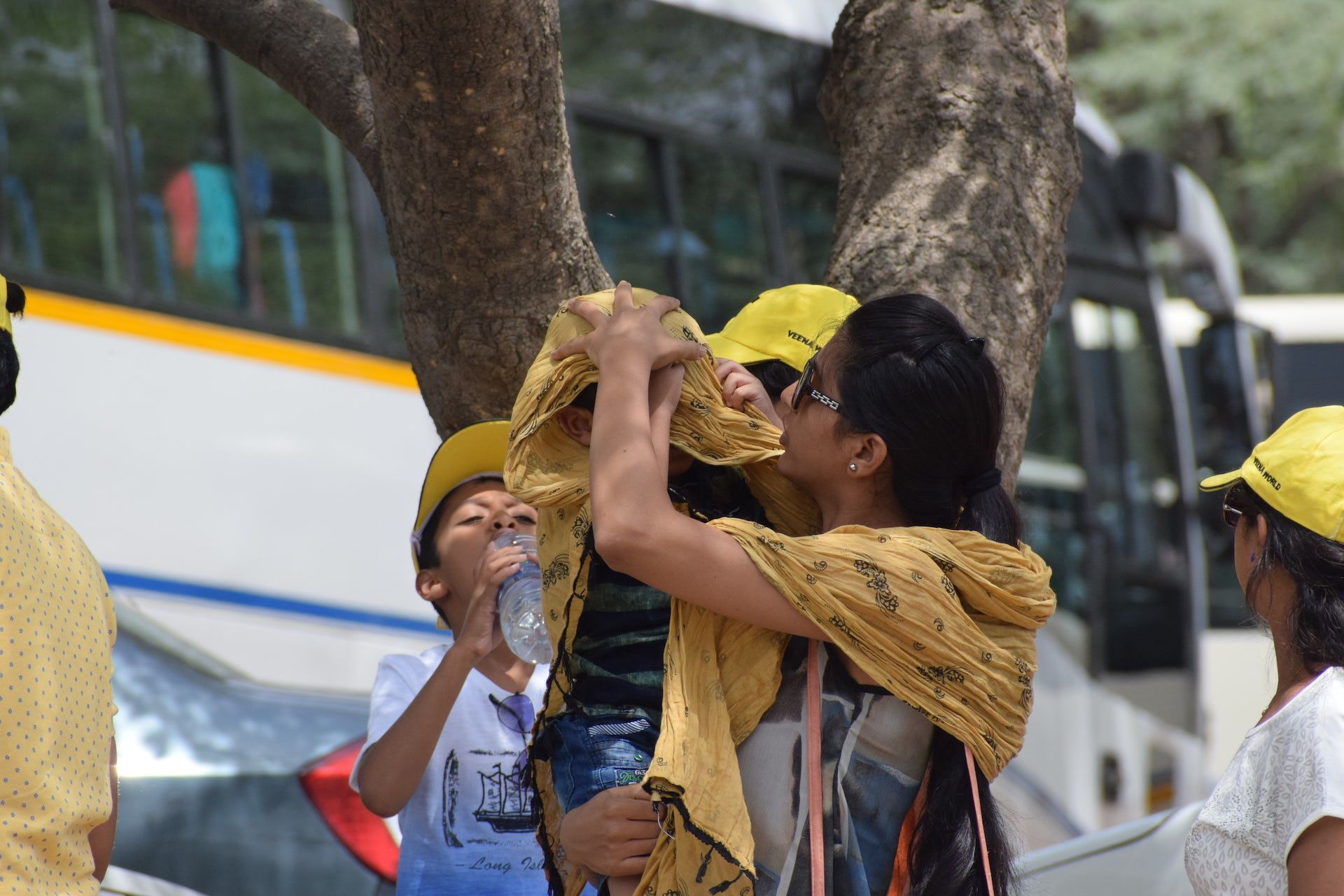 A person covers a child with a blanket to protect them from the sun on a street in India.